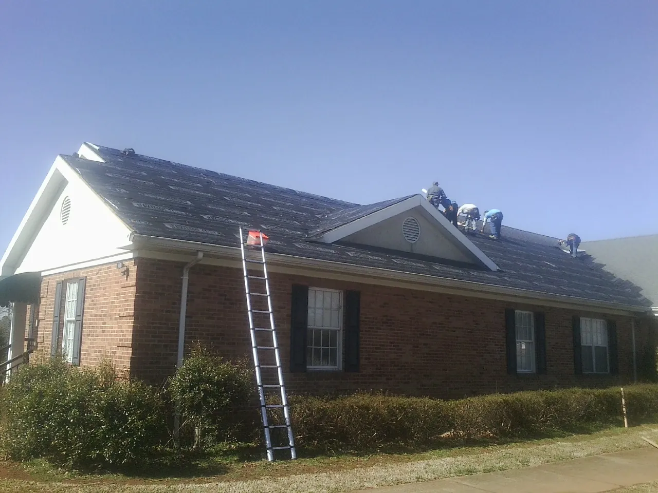 Crew tearing shingles off a brick ranch roof with a ladder set — Metal Roof Repair work by our crew in Sussex
