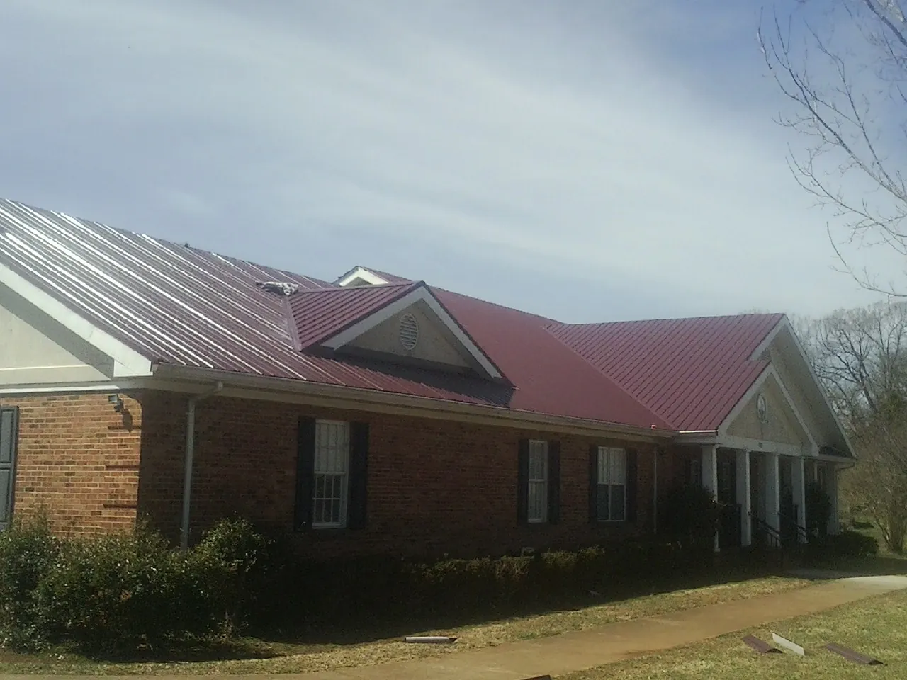 Red metal roof with gabled entries on a long brick building, from a Hail Damage Roof Repair job in Sussex
