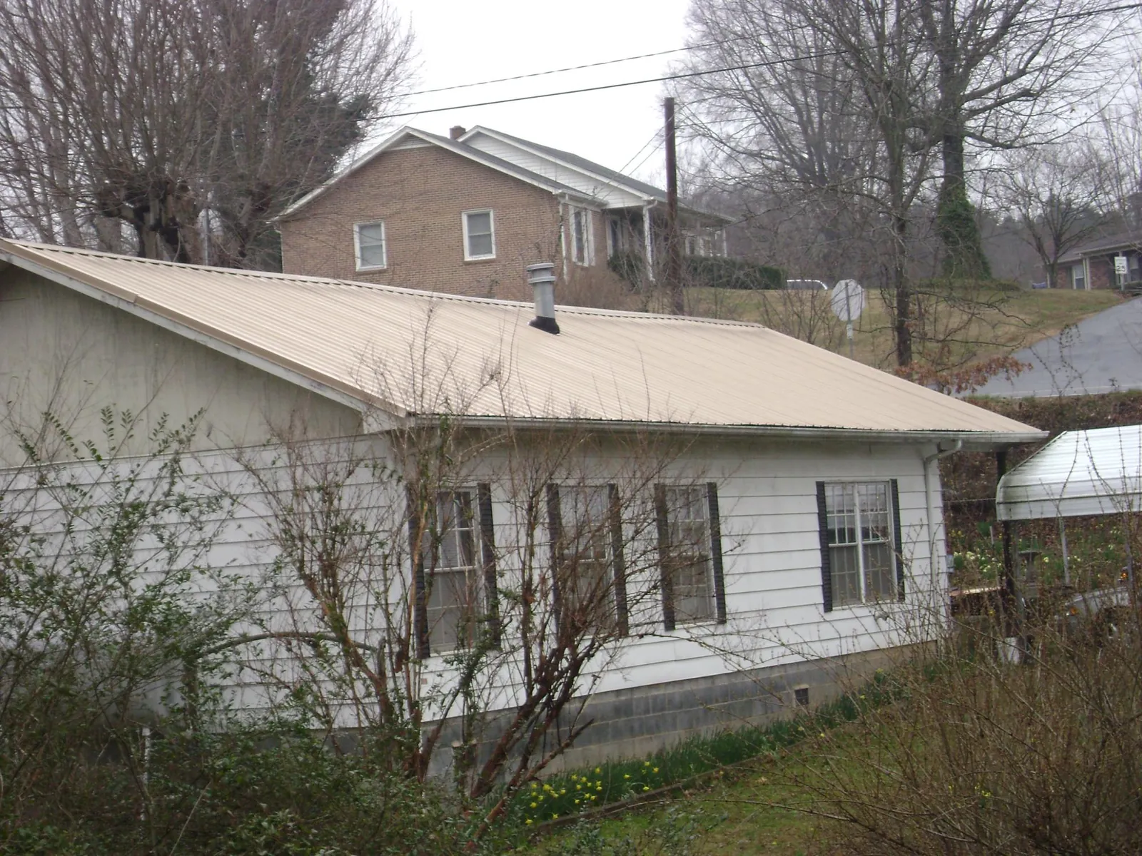 Tan metal roof on a white sided house set into a hillside — Commercial Roofing by Roofing Brothers in Sussex